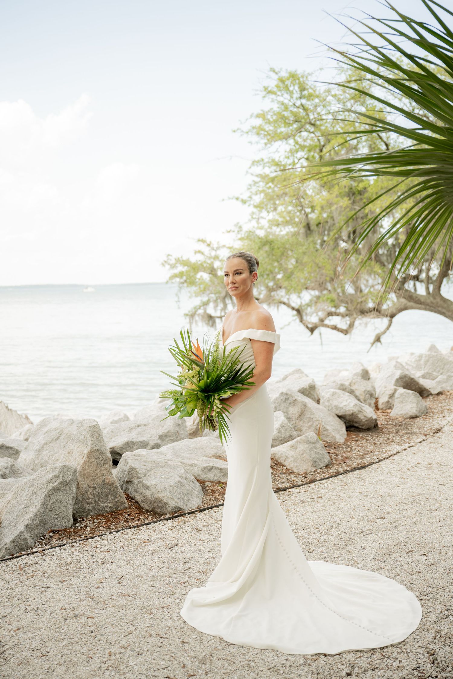 A newlywed couple shares an intimate moment surrounded by palm trees on a sandy pathway during their beach wedding.
