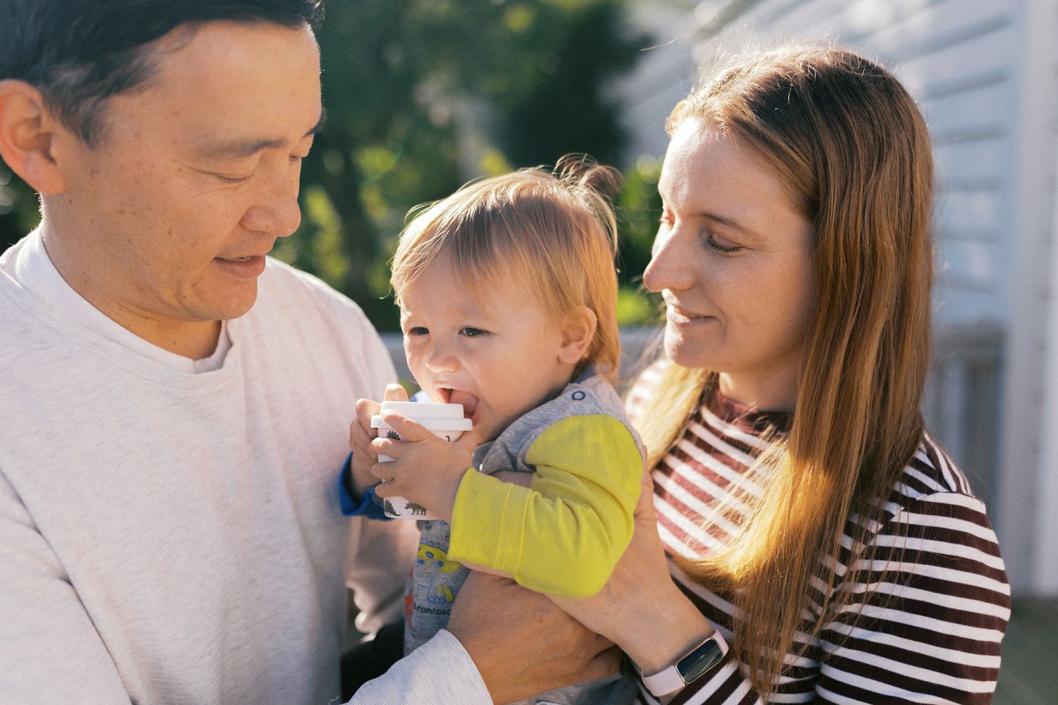 A young family enjoys a tender moment together in bright sunlight outdoors.