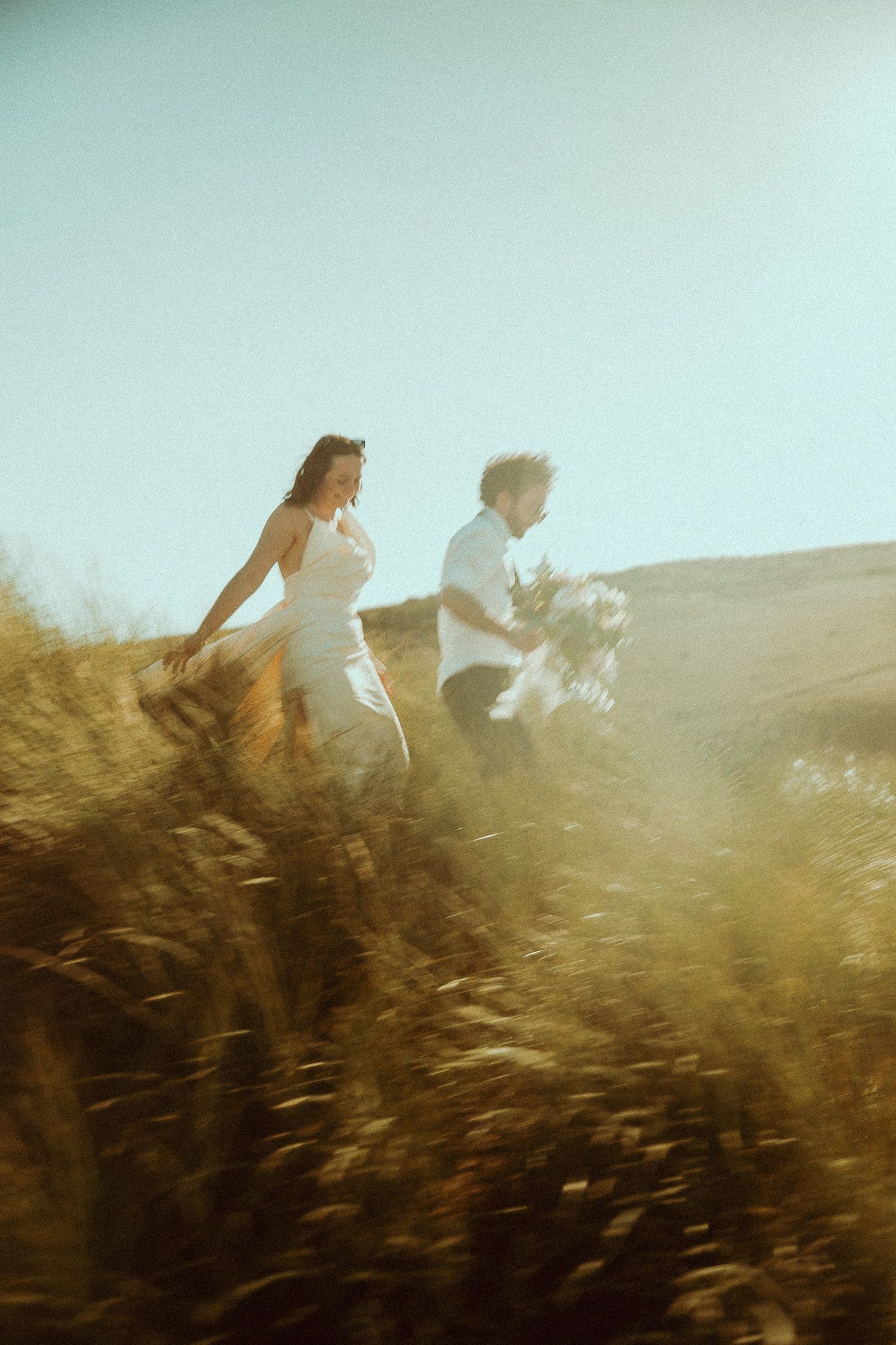 Two figures run through a golden wheat field at sunset creating a dreamy, ethereal silhouette against the sky.