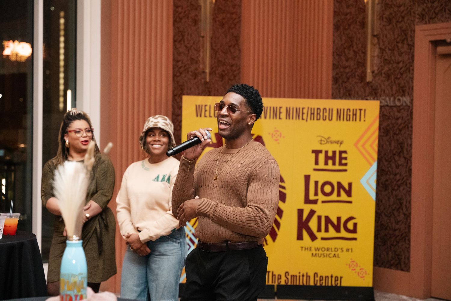 People gather in a theater lobby with ornate decor and yellow Lion King show posters visible on the walls.