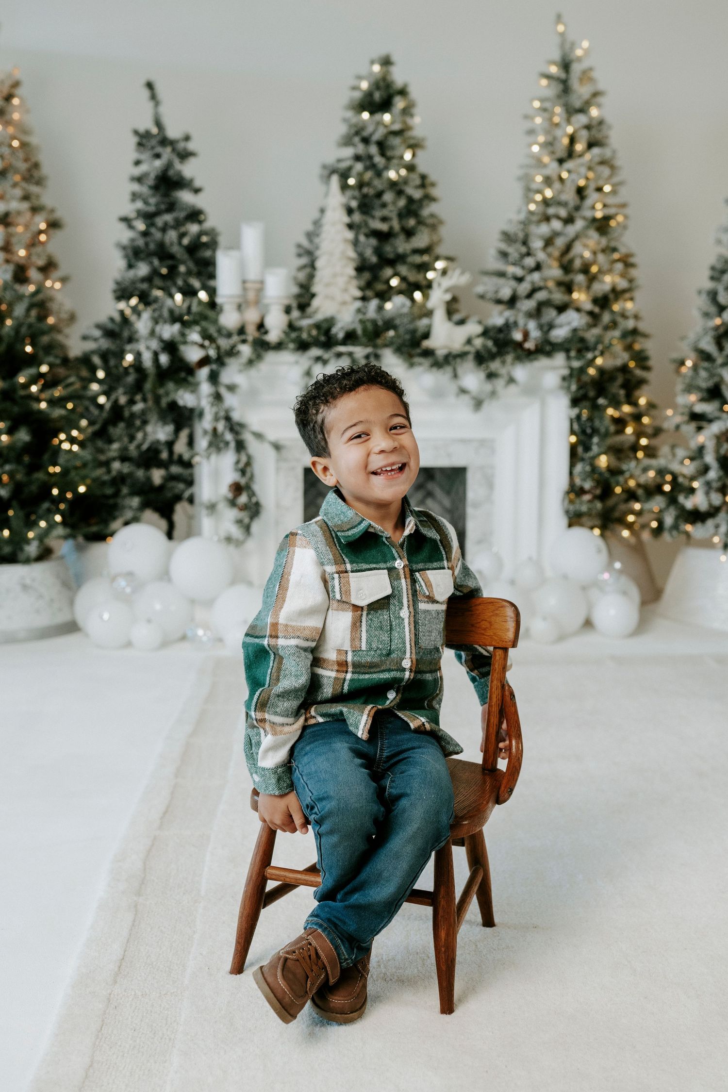 Four sequential photos of a young child sitting in a wooden chair against a backdrop of lit Christmas trees and snow.