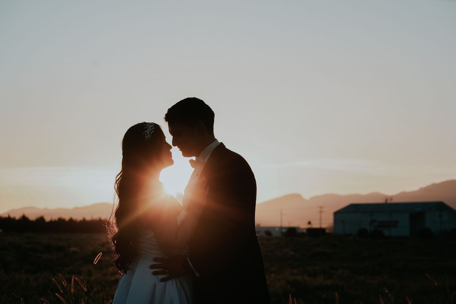 Silhouette of couple embracing during golden sunset with mountains in background creating romantic atmosphere.