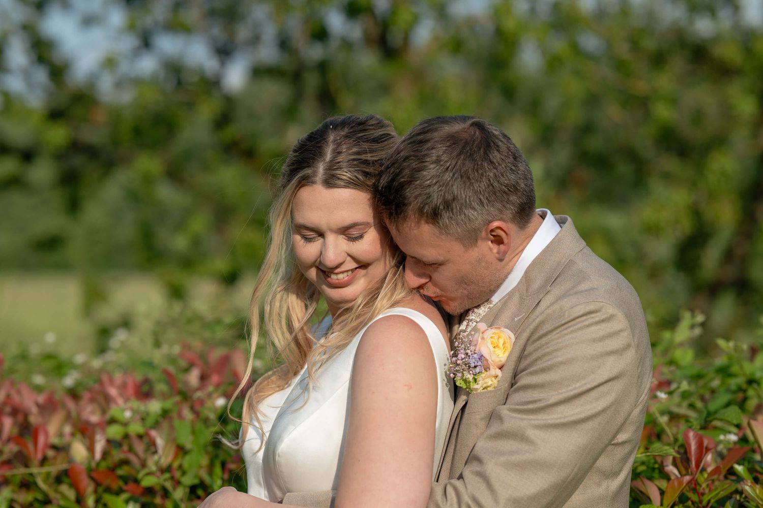 A joyful wedding couple embraces in a lush garden setting with bright summer flowers.