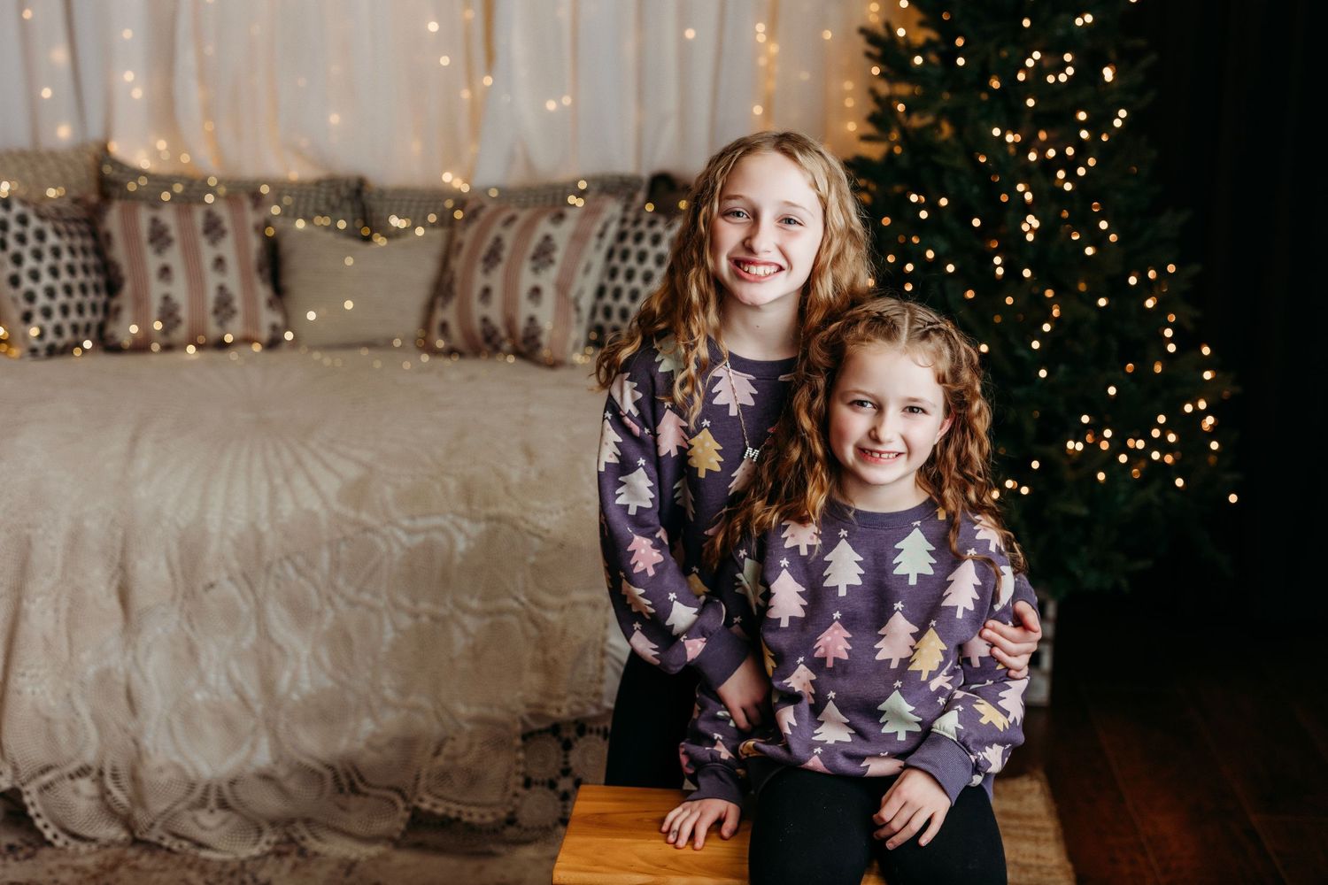 Festive holiday portraits with twinkling Christmas lights and pine tree decorations in the background.