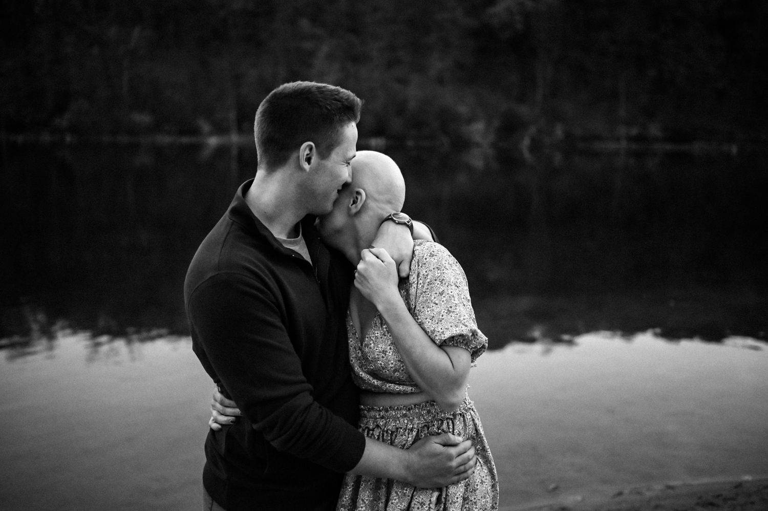 A romantic black and white photo series showing a couple embracing by a lake at sunset.