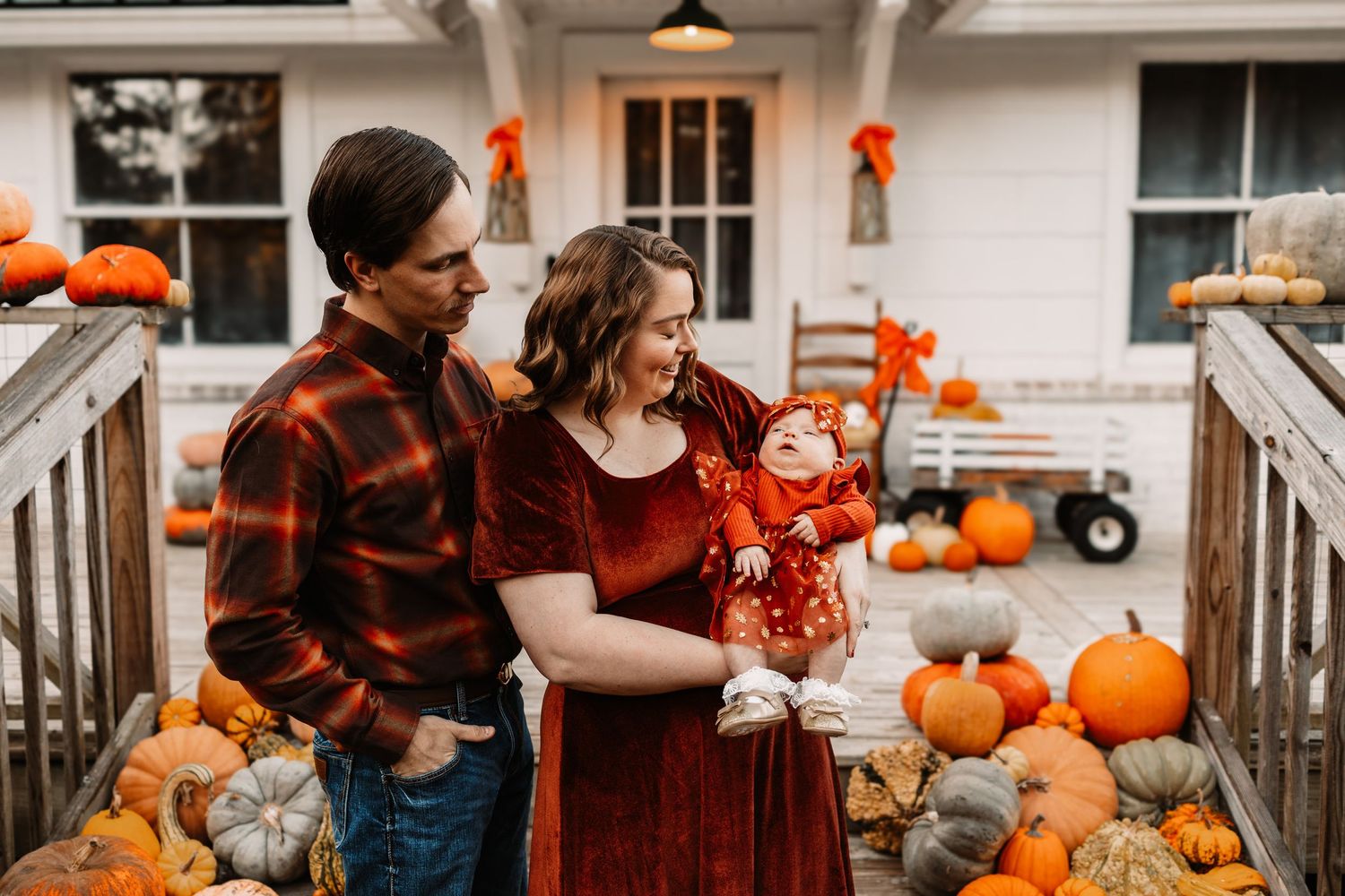 Couple in matching rust and plaid fall outfits smile at their baby during a family photo session in Knoxville, TN.