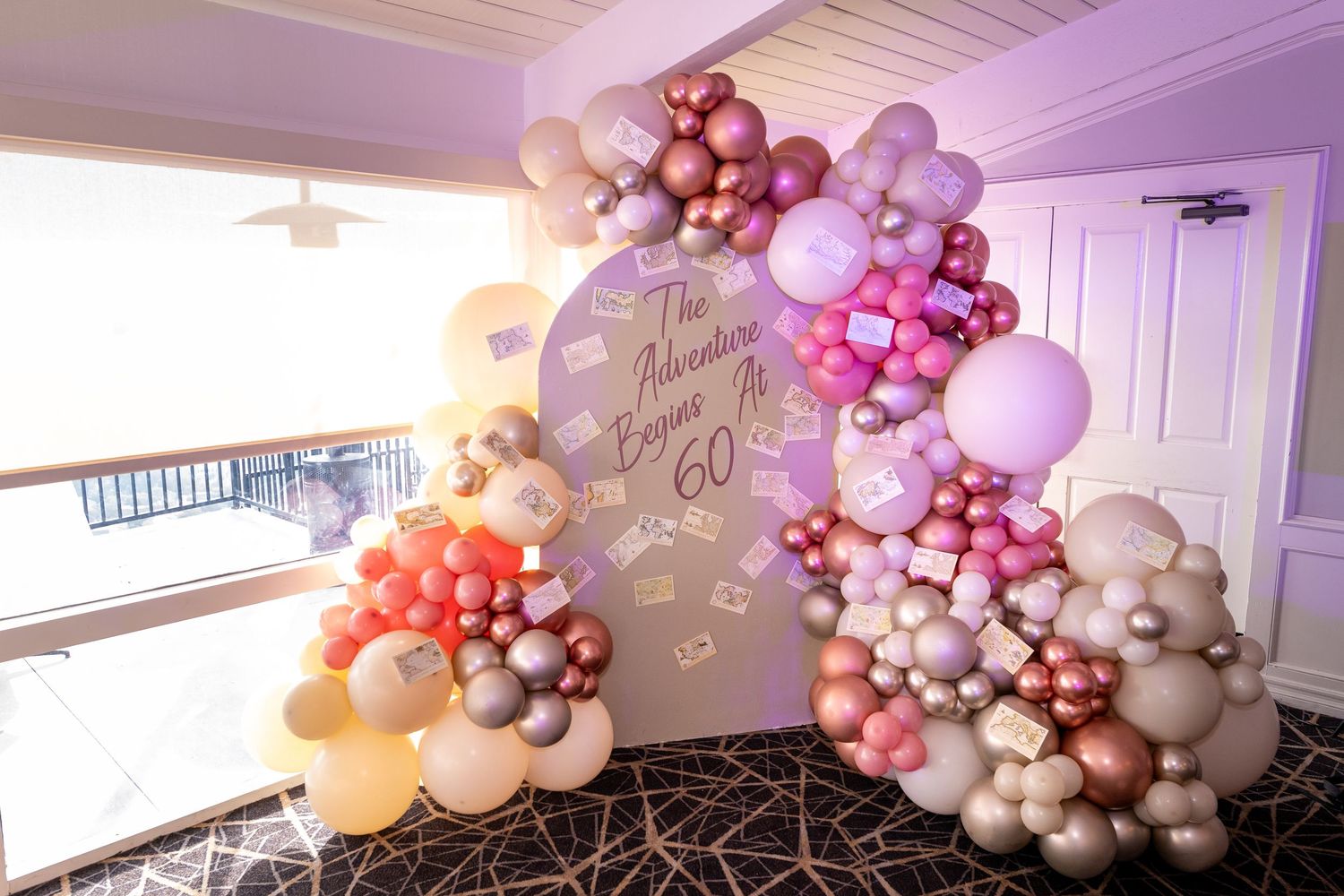 Elegant 60th birthday balloon arch display in pink, rose gold, and cream tones with decorative signage backdrop.