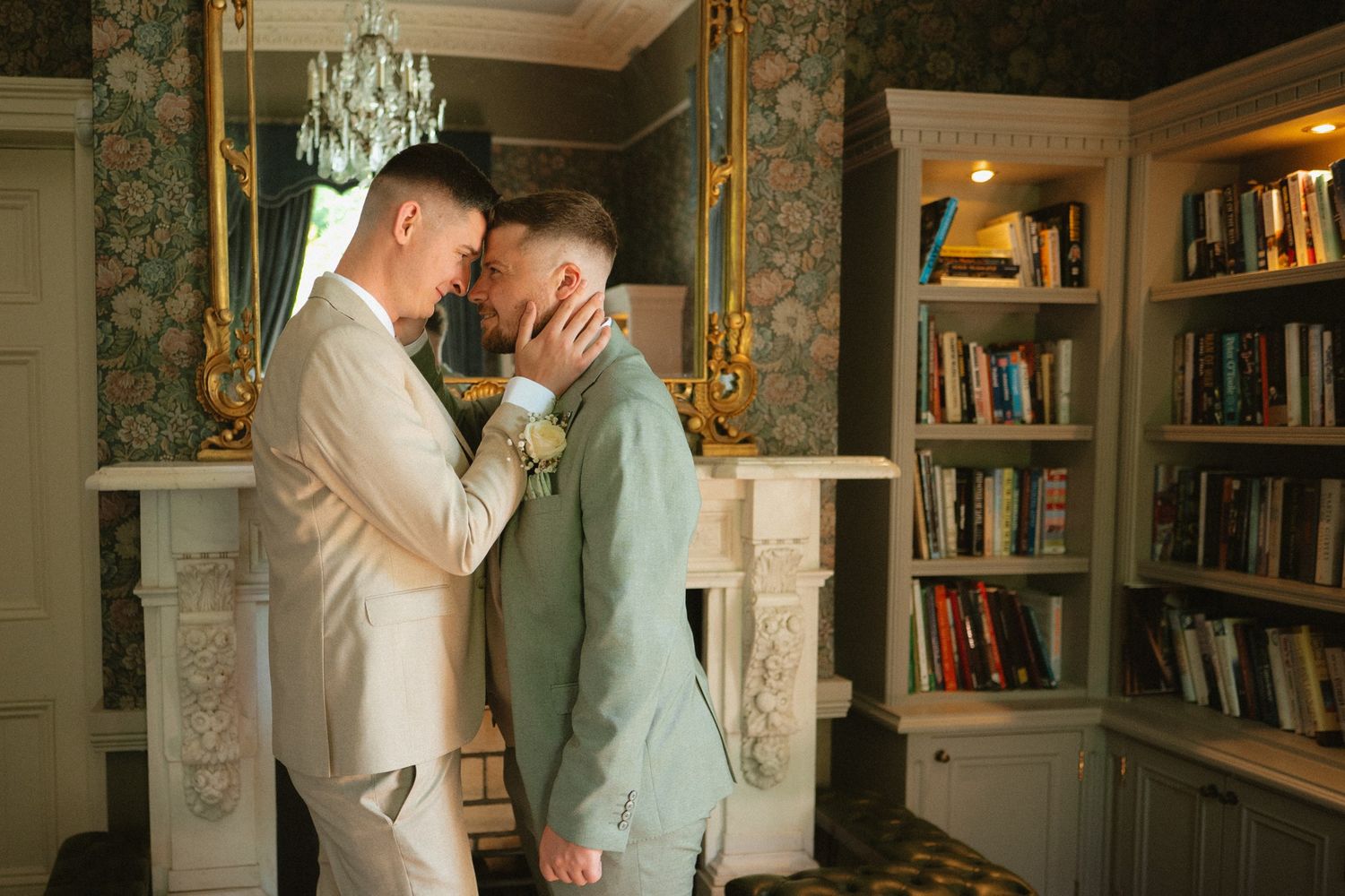 Ciaran and Ross embracing beside the bookshelves on their wedding day at Tulfarris.