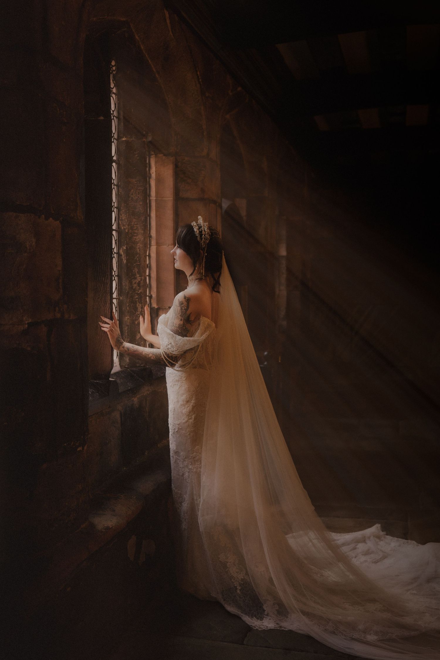 Black and white photo of a couple sharing a romantic kiss near a stone church wall on their wedding day.
