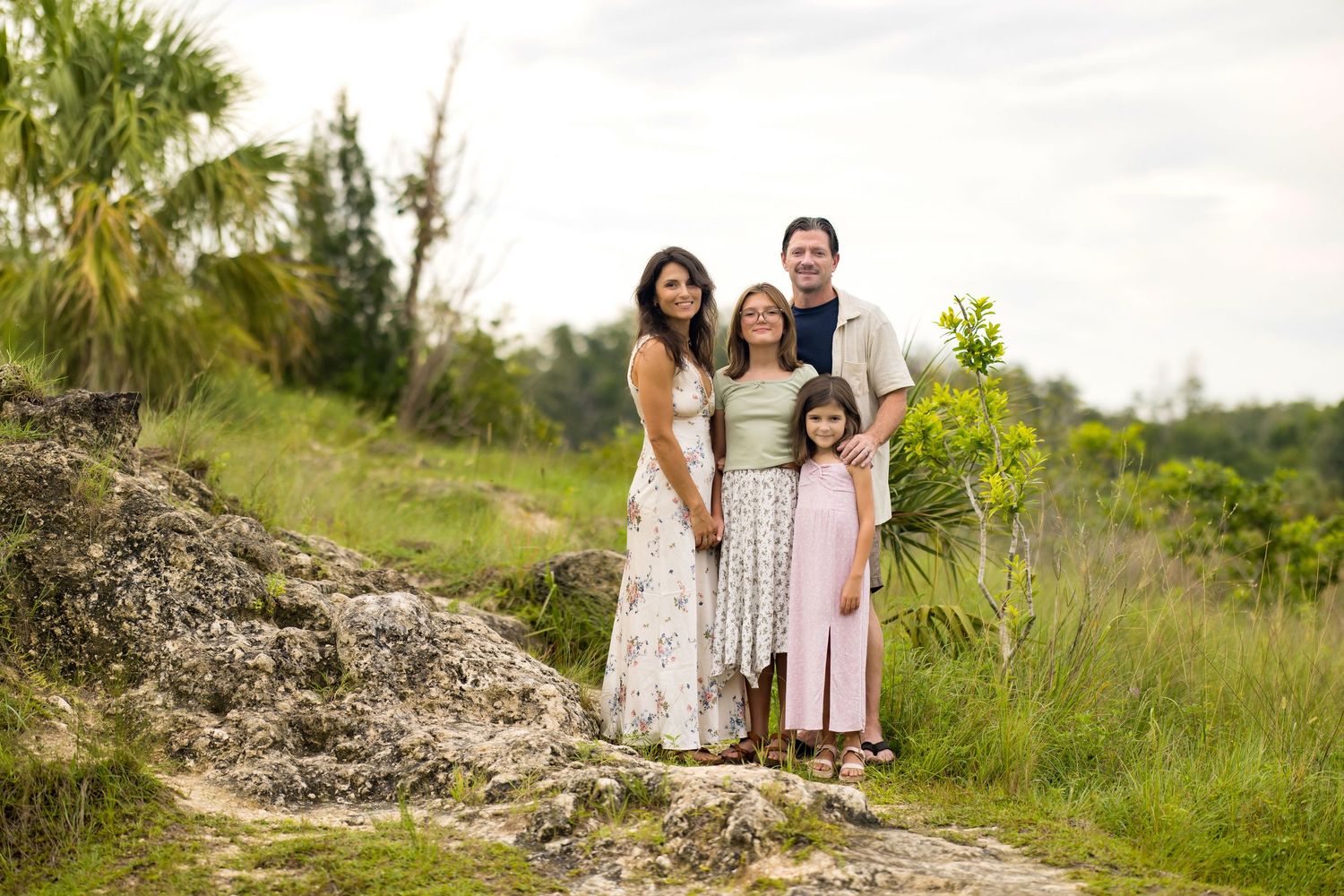Family of four smiling together outdoors on a rocky path surrounded by lush green tropical vegetation.