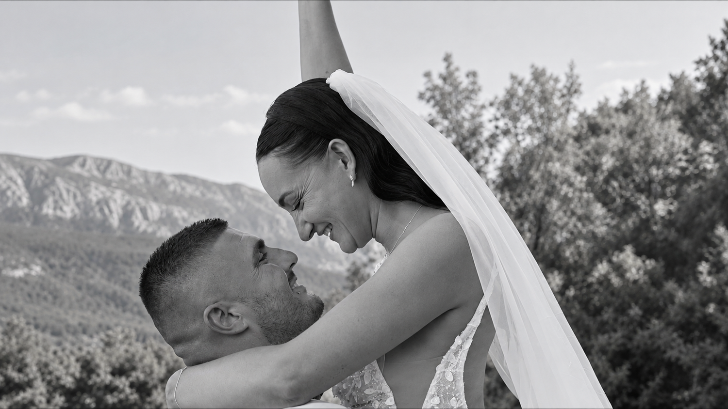 Manon et Kevin sourient, enlacés pendant leur mariage du 8 août 2026, photographiés en noir et blanc.