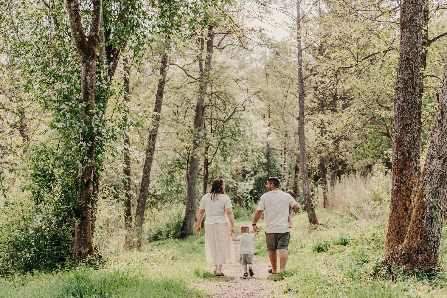 A couple walks with their small child on a wooded path during a sunny day in nature.