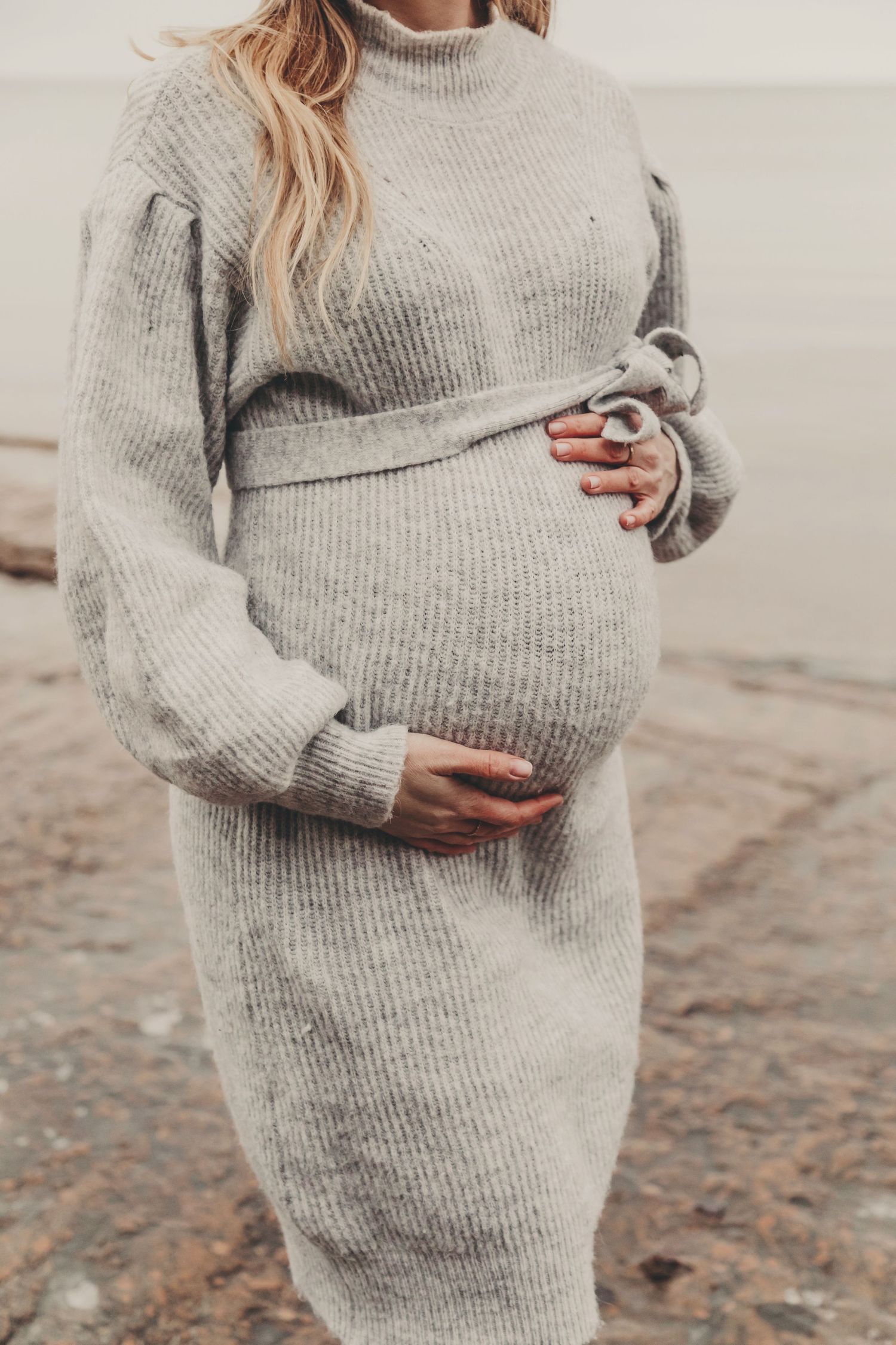 Close-up view of a grey ribbed sweater dress highlighting a pregnant belly against a neutral background.