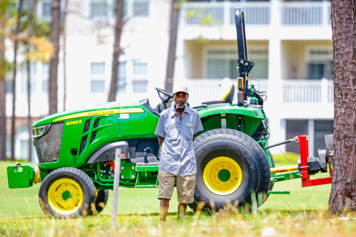 Person standing proudly next to a bright green John Deere tractor on a grassy lawn.