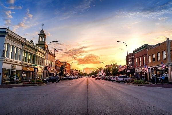 A breathtaking sunset over downtown Geneva, Illinois, with warm hues of orange, pink, and purple illuminating the sky.