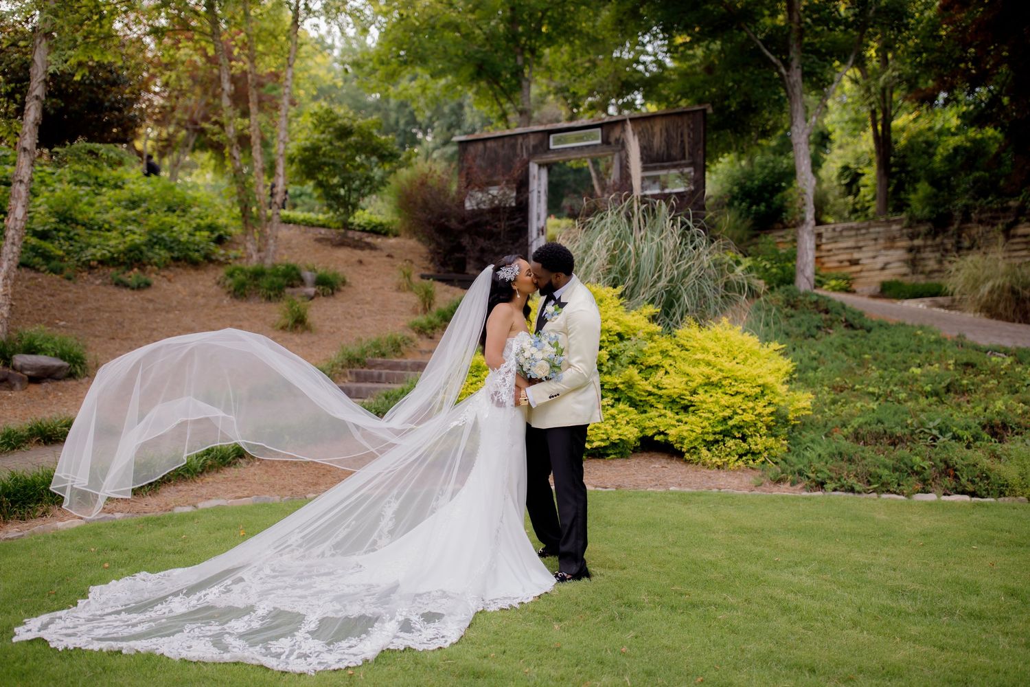 Bride's veil flows dramatically in the wind during garden wedding photo session.