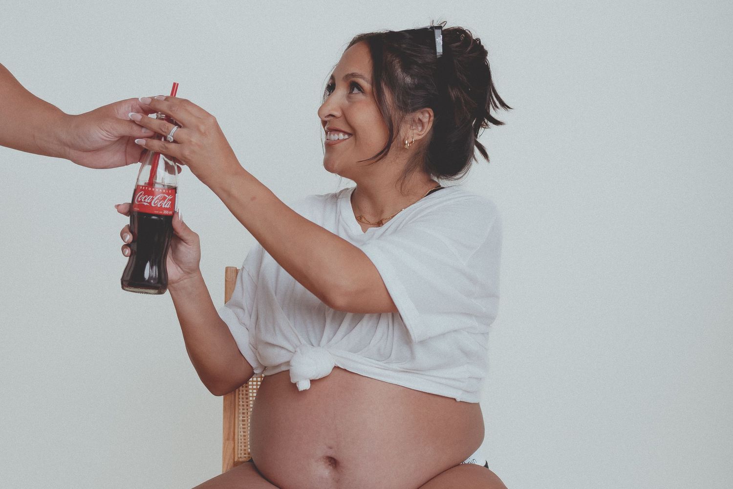 Playful maternity photo with a bottle of soda being shared against white background.