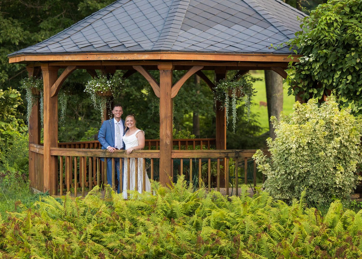 Newlyweds share an intimate moment outdoors with autumn foliage and rustic architecture in background.