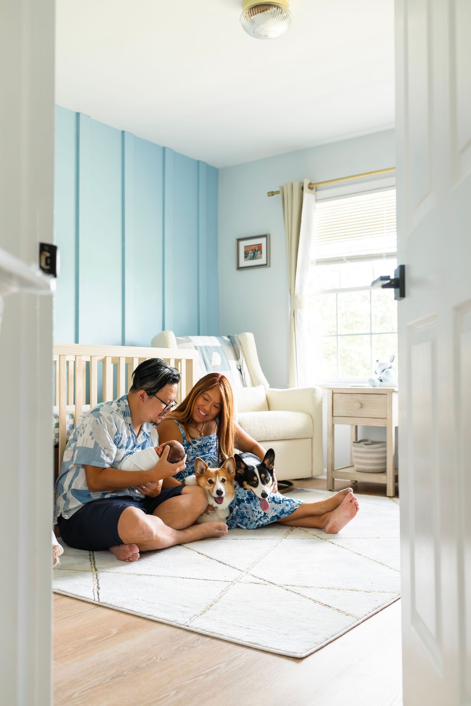 Two people sit on floor of nursery with dogs while enjoying family time together.