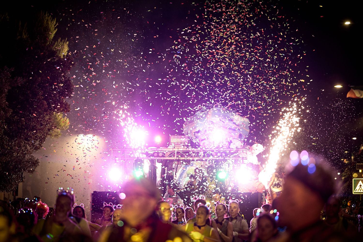 Vibrant purple fireworks and confetti illuminate a nighttime concert crowd.