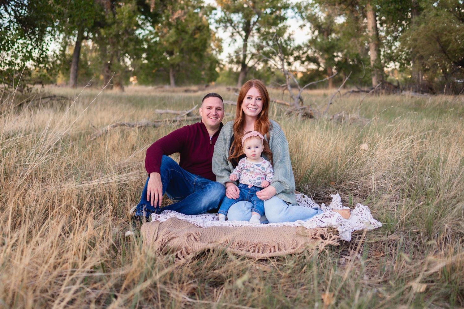A family of three sitting on a blanket in a grassy field during golden hour.