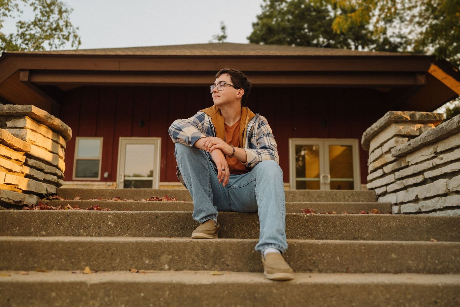 Person in brown jacket and jeans sits contemplatively on concrete steps during golden hour.