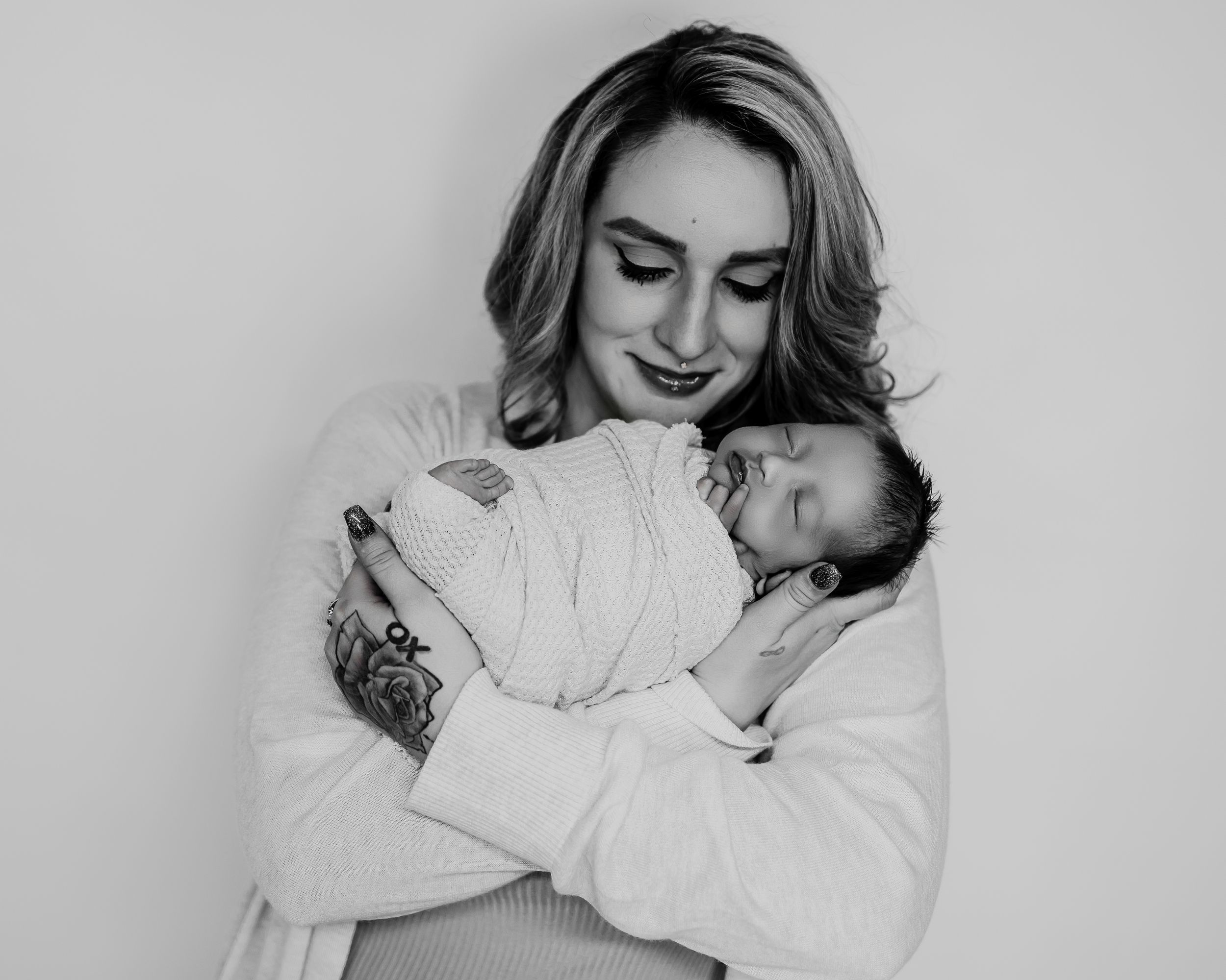 Black and white photo of tender moment between parent and sleeping newborn baby wrapped in swaddle blanket.