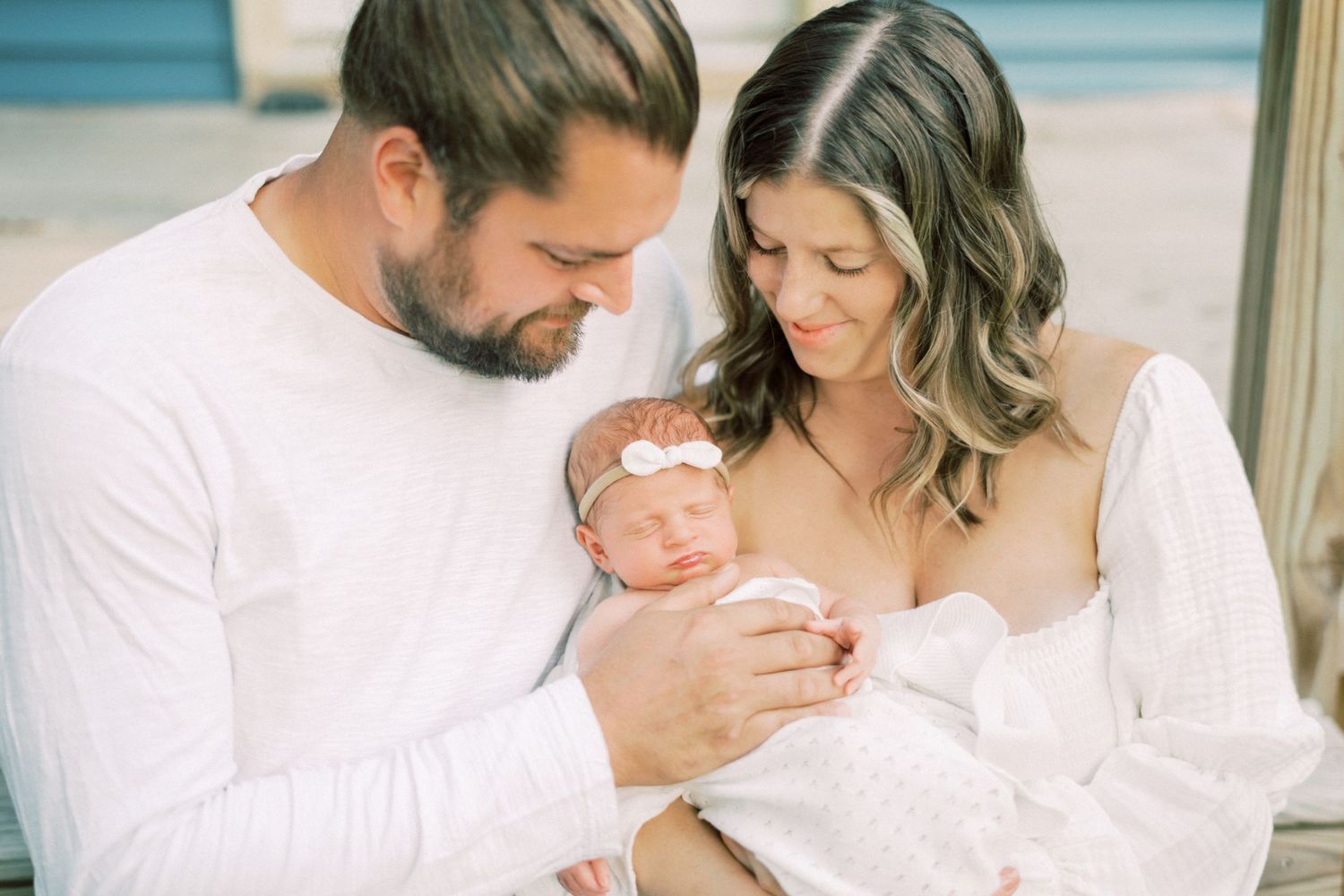 Intimate family moment with newborn baby wearing pink headband in a warm indoor setting.