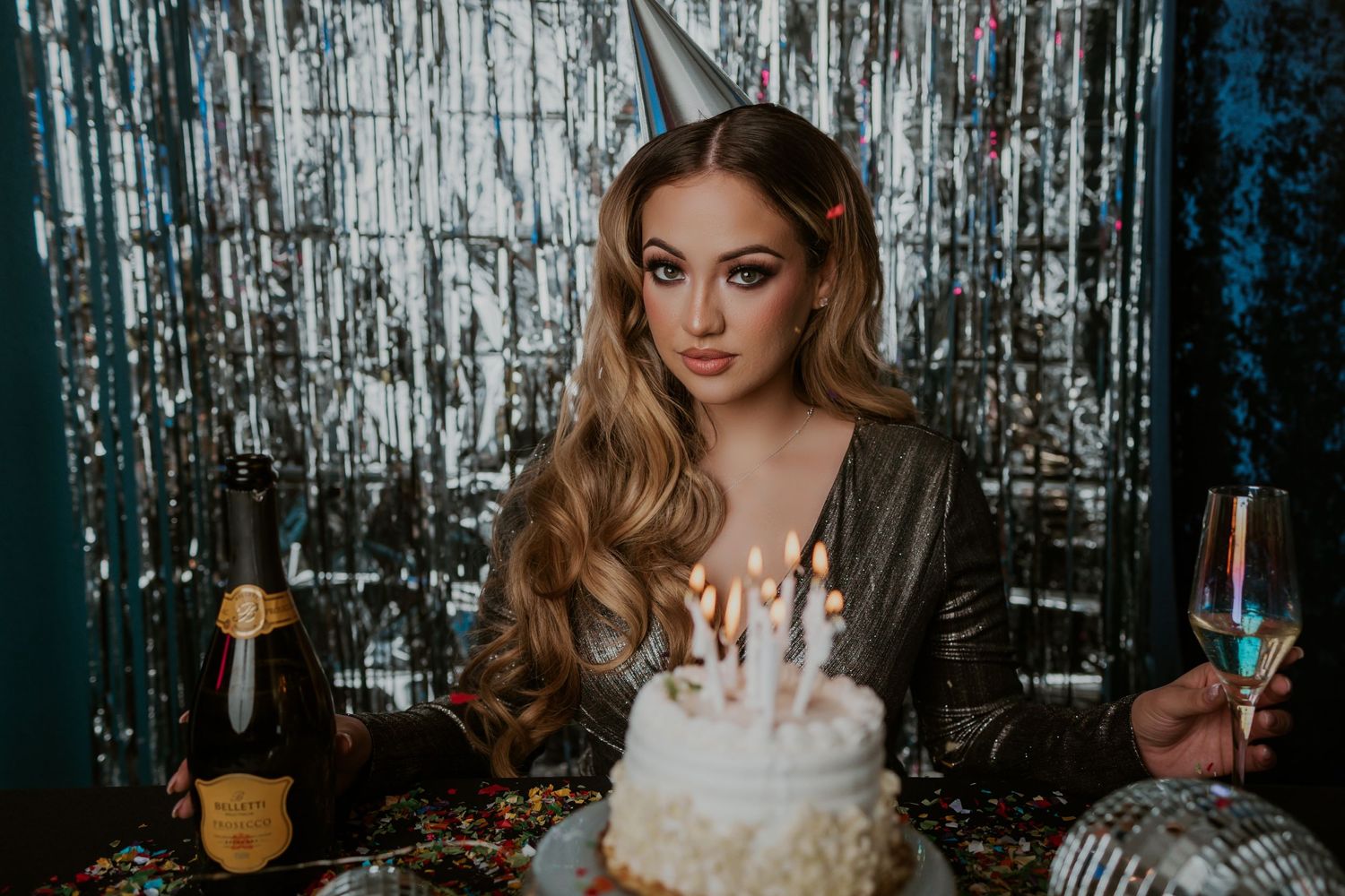 A birthday celebration scene with a lit cake and silver tinsel backdrop.