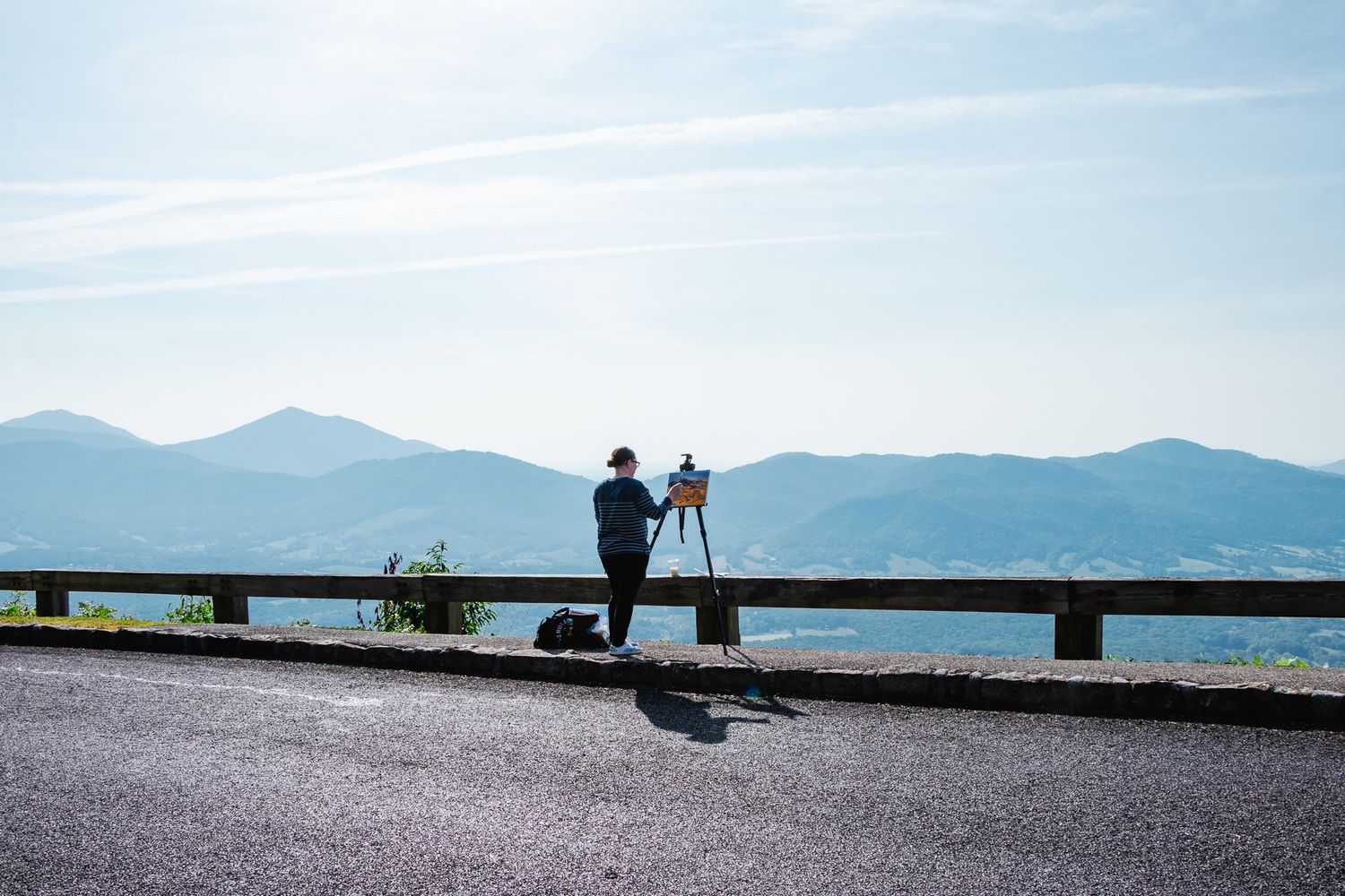 A wide view of an artist painting at an overlook along a mountain road, with expansive Blue Ridge mountains stretching across the horizon