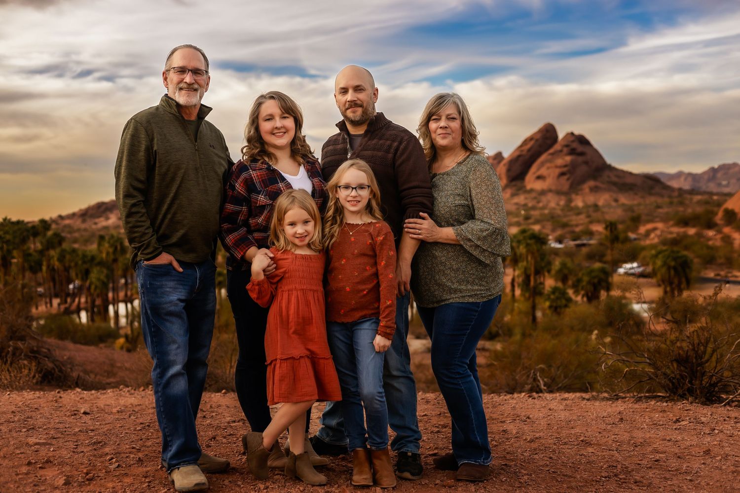 A family poses together on red rocks at sunset with Camelback Mountain in Phoenix visible in the background.