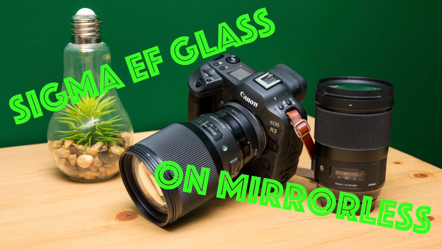 Photography equipment setup with Sigma EF Glass lens and mirrorless camera on wooden surface with green background.