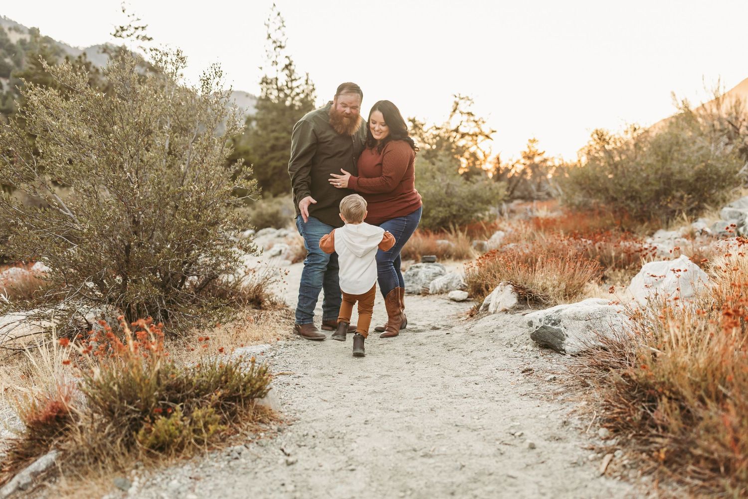 A family walks together on a desert hiking trail during golden hour with desert brush and rocks surrounding them.