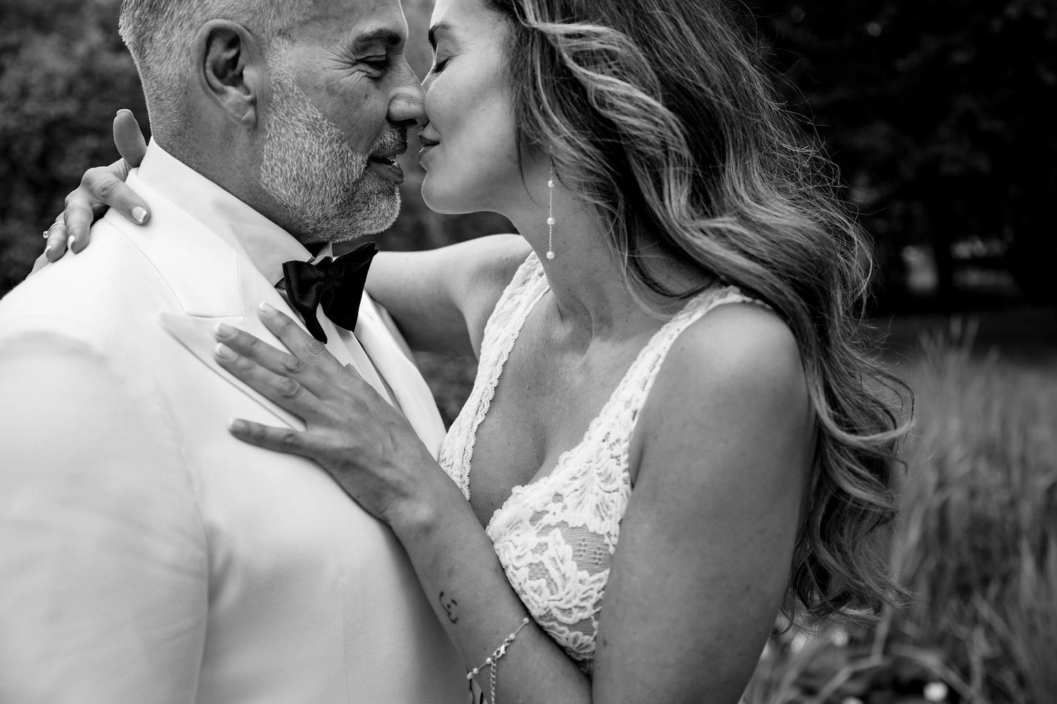 A tender black and white portrait capturing an intimate kiss between a couple in formal wedding attire outdoors.