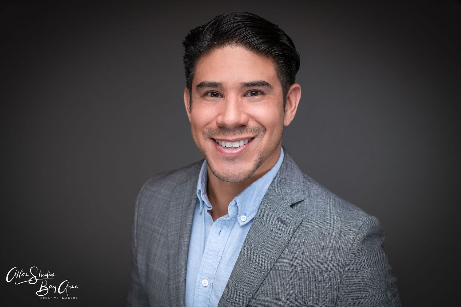 Professional headshot of person in gray suit jacket and blue shirt against dark background.
