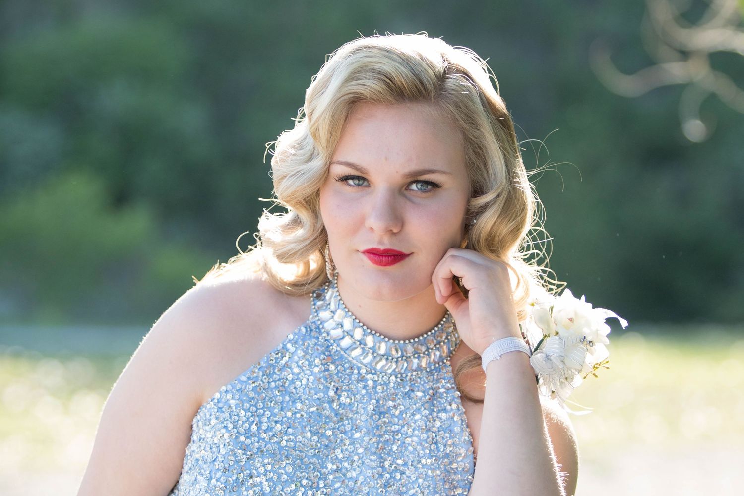 A person in a sparkly blue dress poses outdoors in natural sunlight.