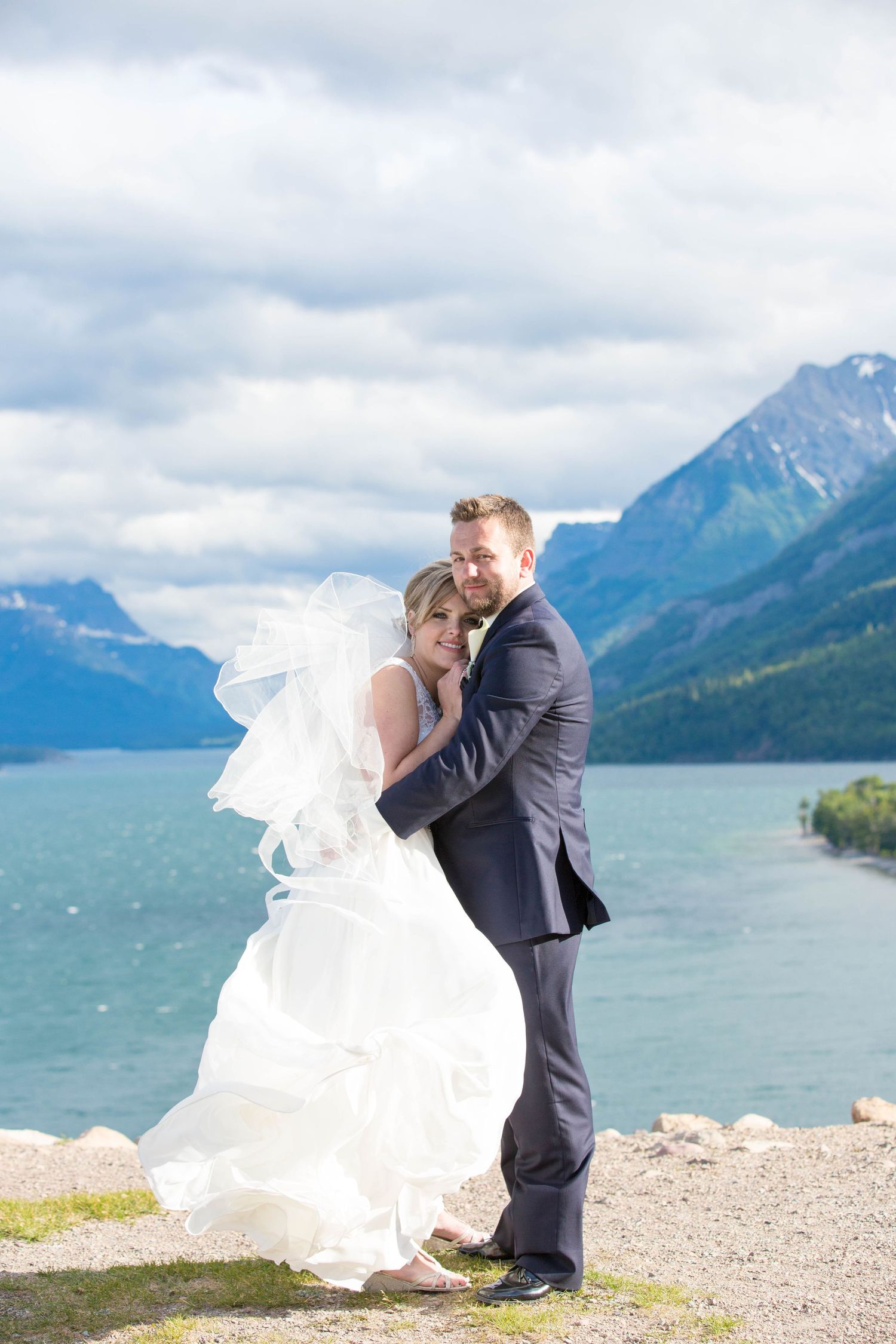 Dramatic wedding photos with mountain lake and cloudy sky backdrop.