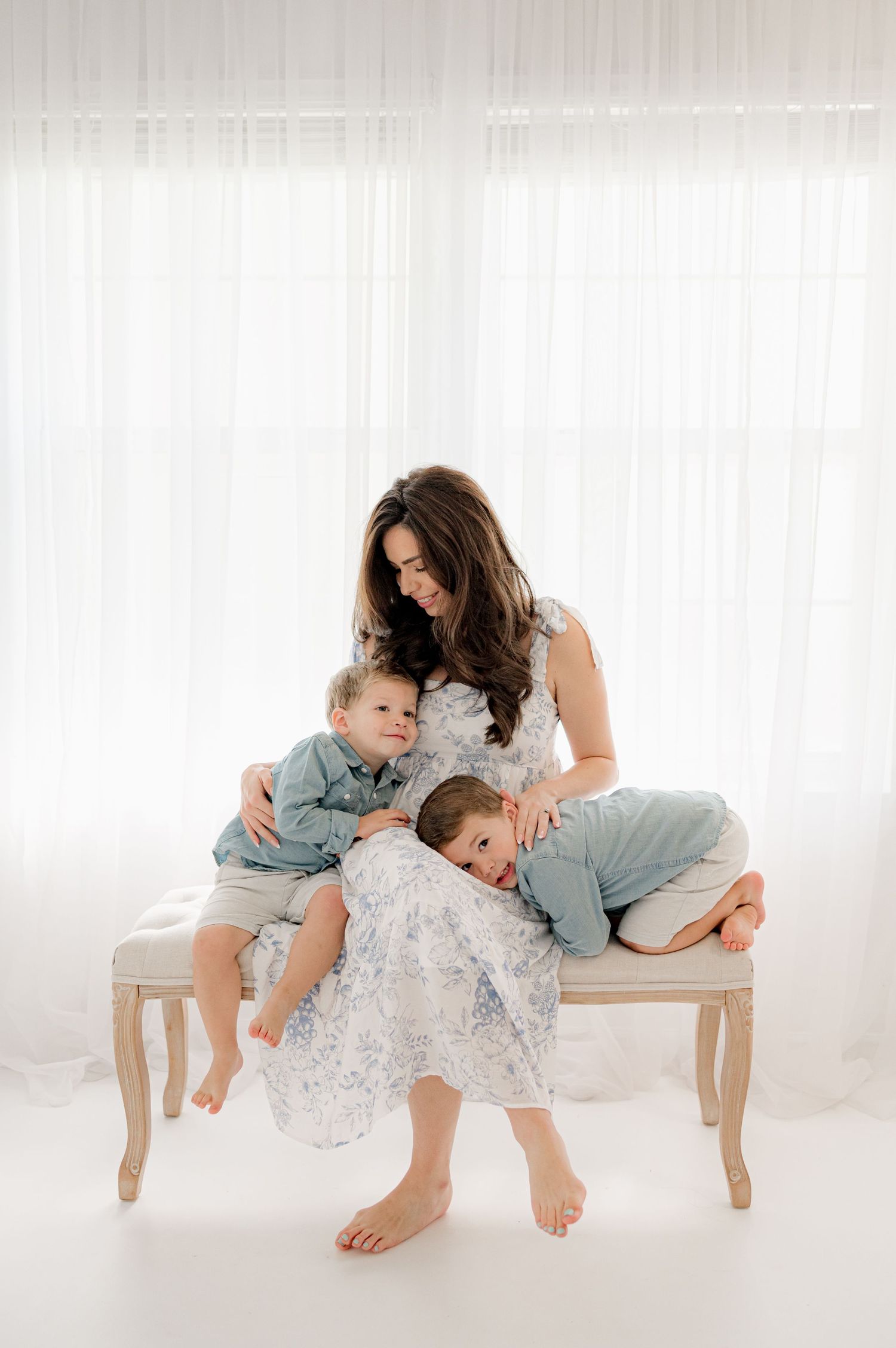 Family portrait on bench showing tender moment between parent and children in light airy setting.
