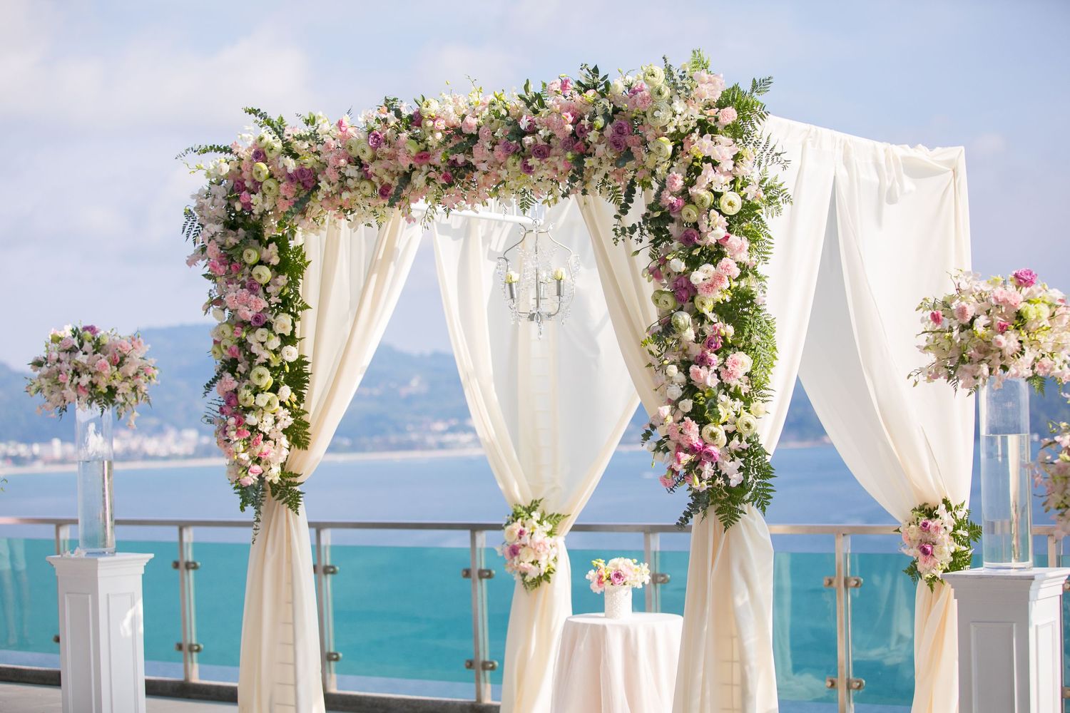 Elegant beach wedding arch decorated with pink and white flowers and flowing white fabric.
