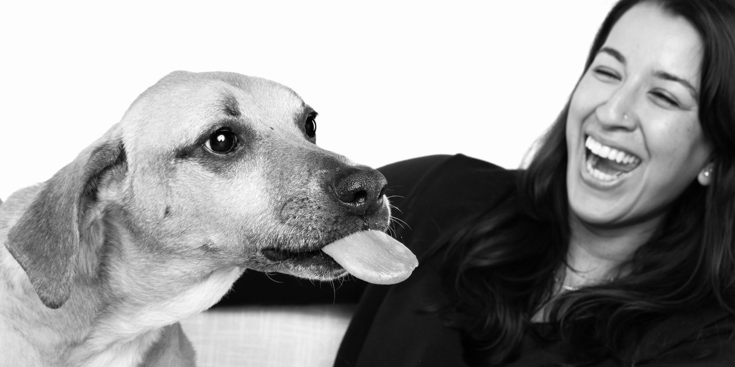 A woman laughing joyfully next to a yellow Labrador dog with tongue out, black and white photo.
