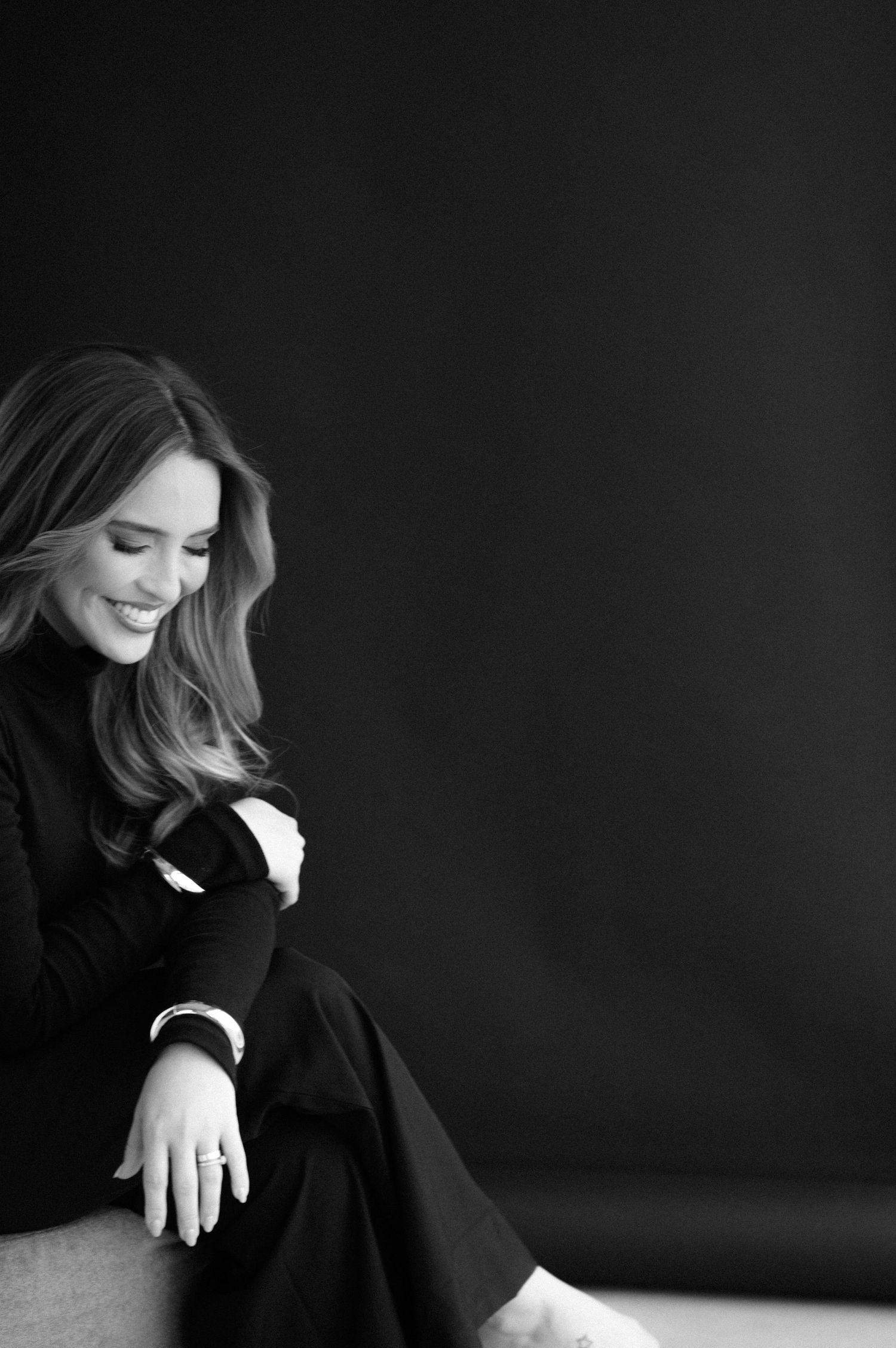 Black and white portrait of someone in dark clothing laughing while sitting.
