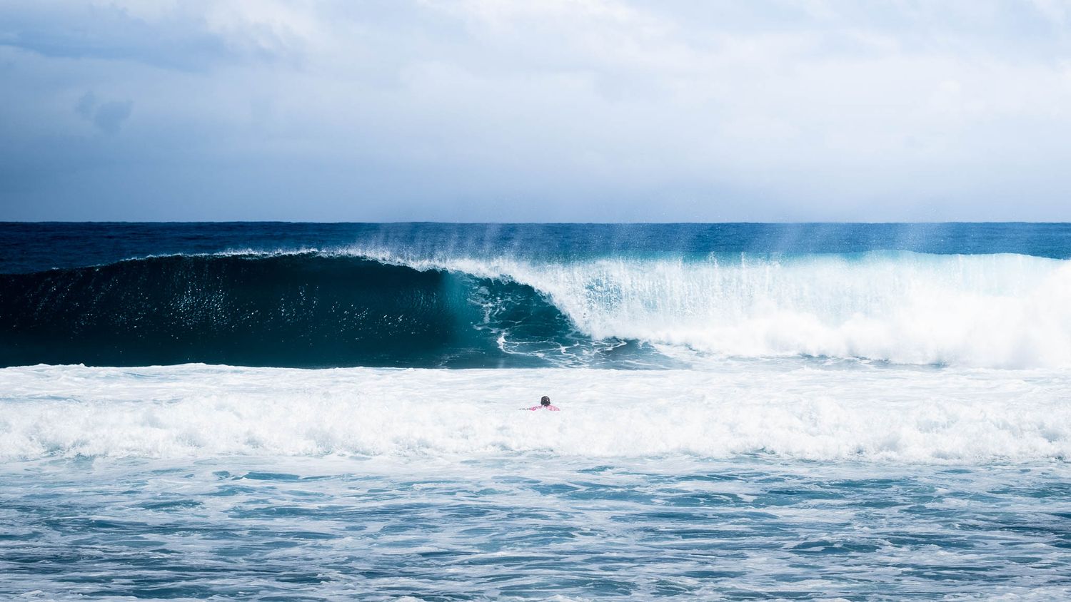 Massive ocean wave breaking with white spray in dark blue waters.