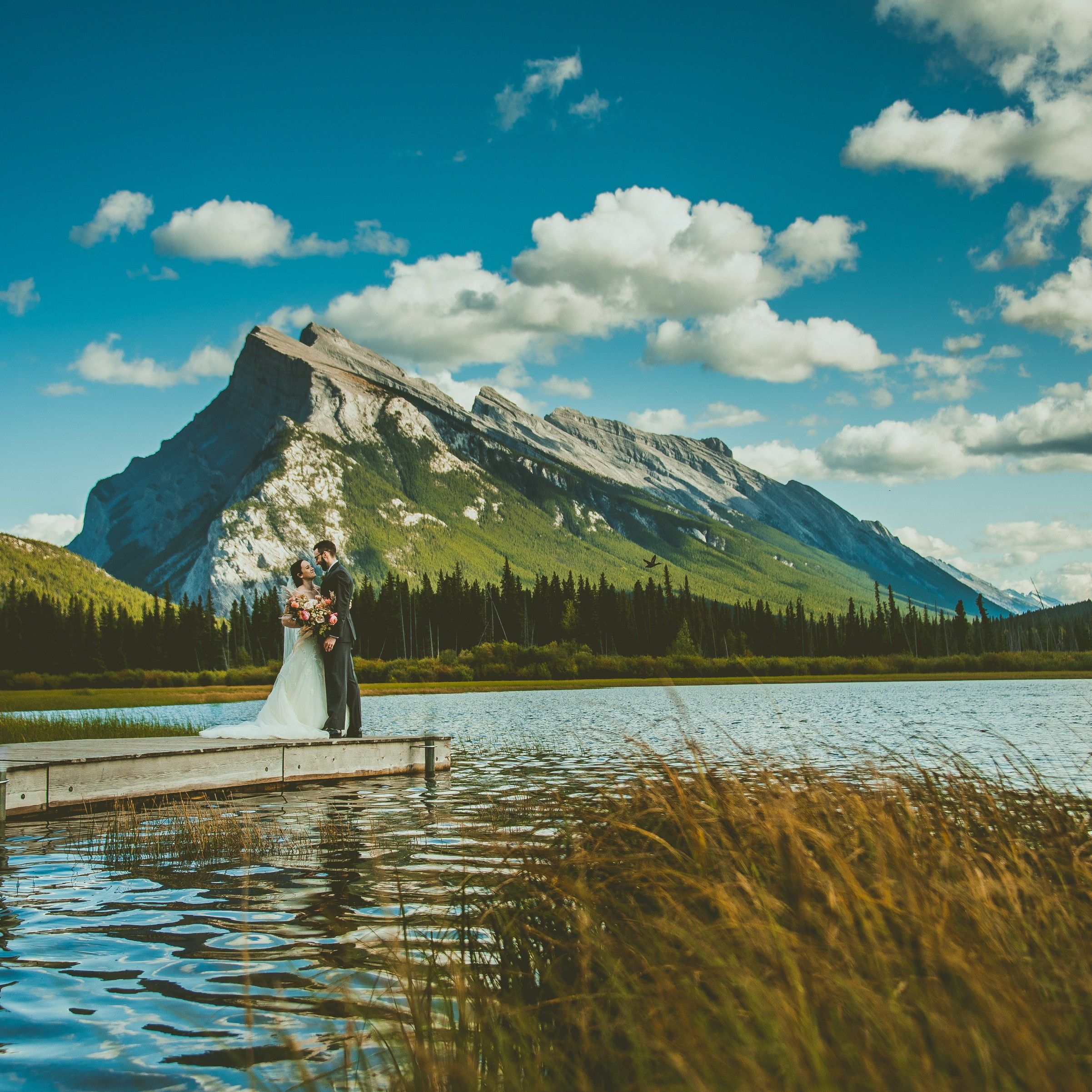 Wedding couple on dock at Lake Vermillion with Mount Rundle in background. Banff Elopement Micro Wedding Photographer