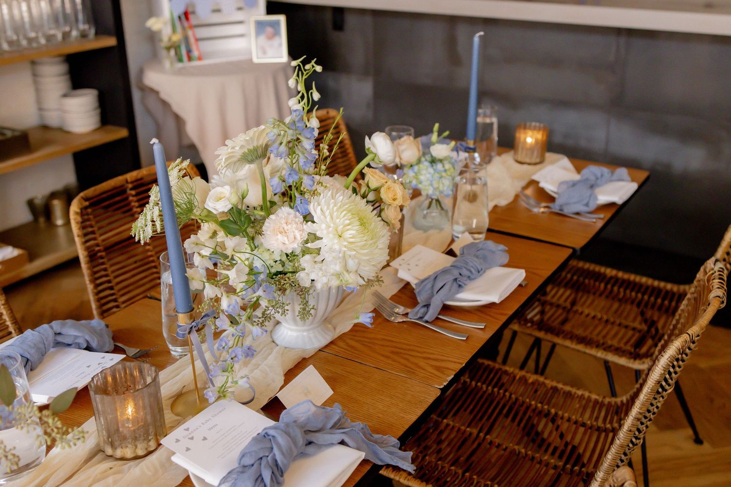 Elegant wedding table setting with white floral centerpiece, blue taper candles, linen napkins, and glassware on a wooden table.