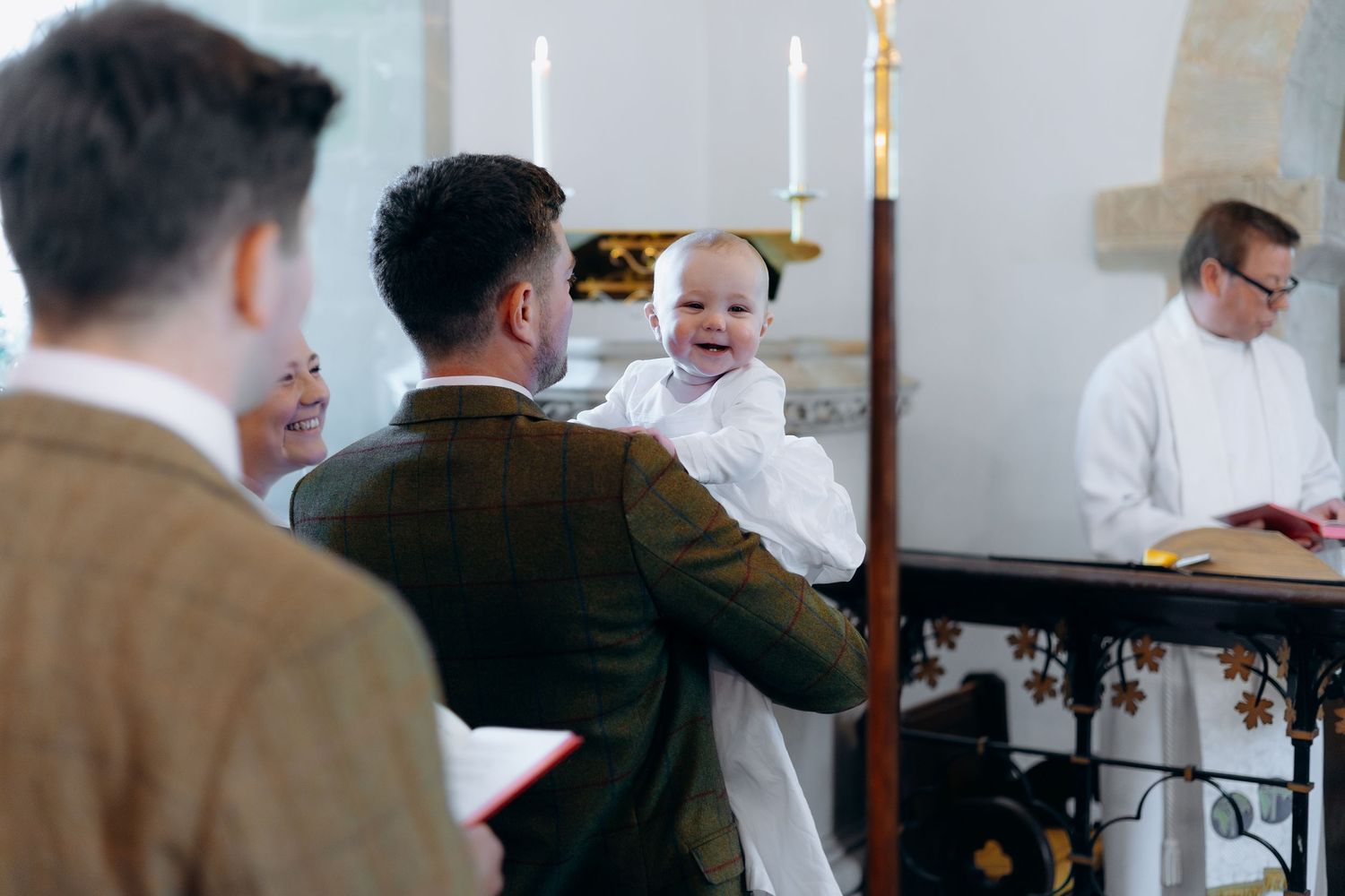 A priest performs a baptism ceremony on an infant held by the father in a church setting.