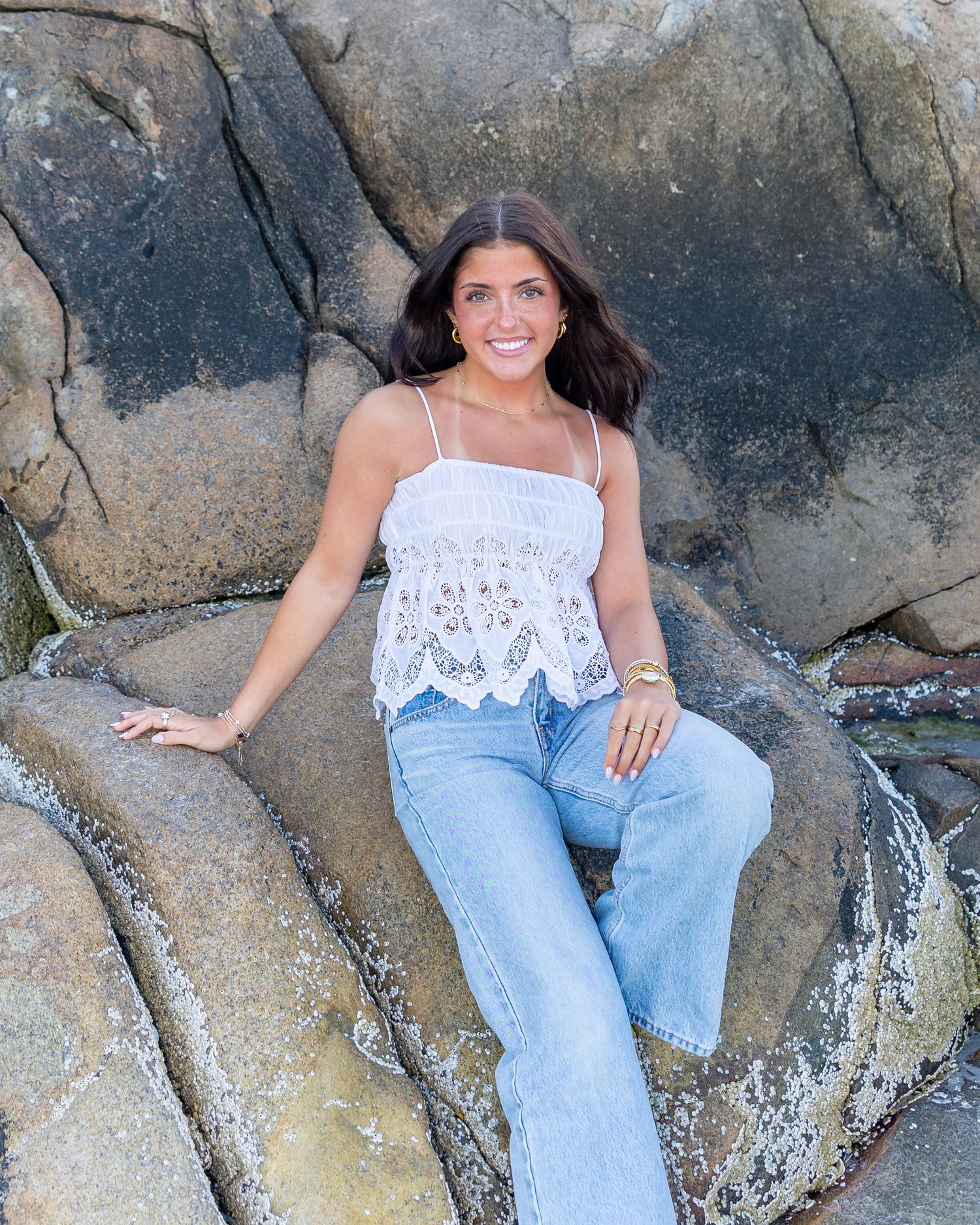 High school senior in poses on large rocks at Wingaersheek Beach in Gloucester, MA for yearbook portrait session at sunset golden hour.