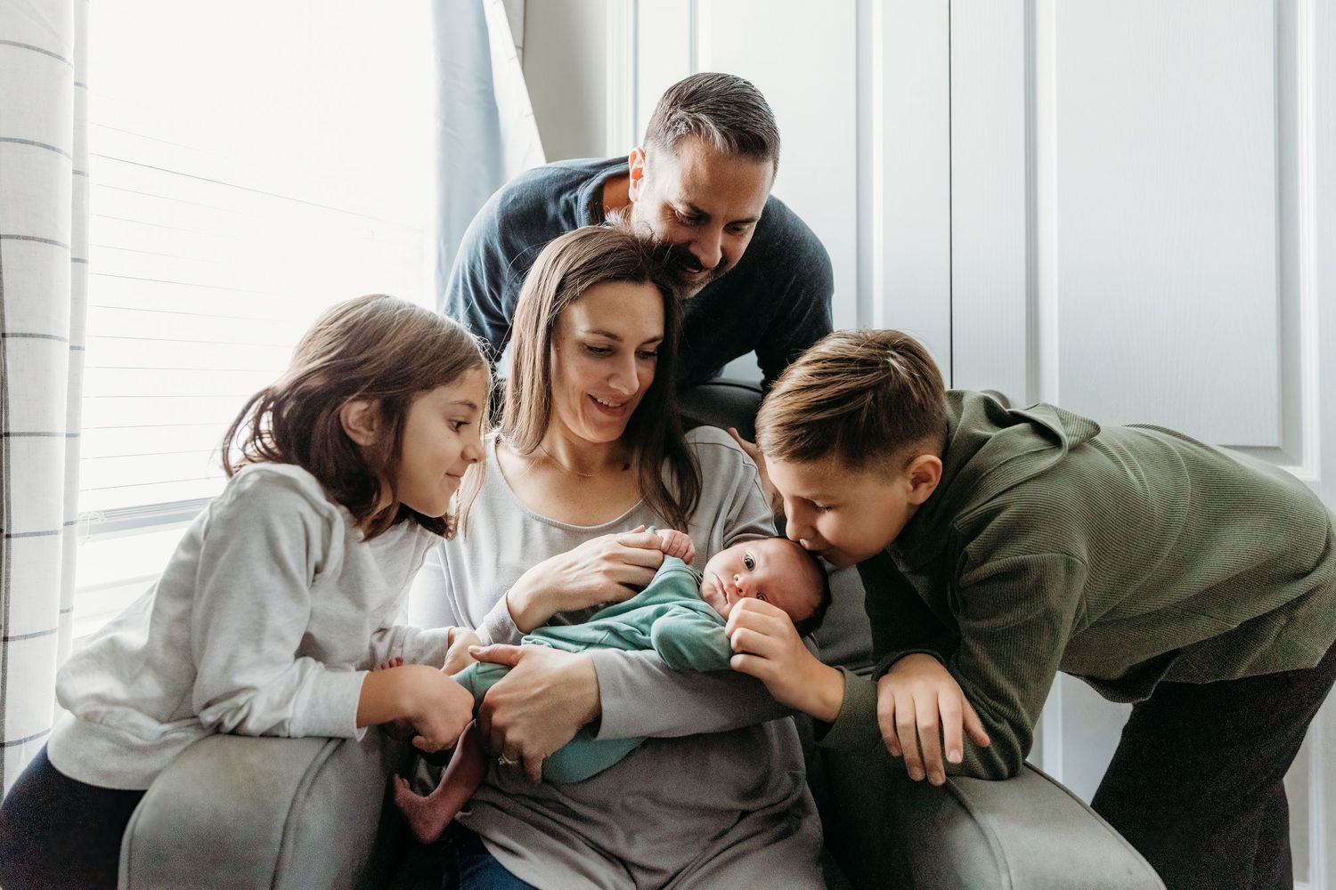 Family of five gathered together admiring their newborn baby, sharing a tender moment of love and joy.