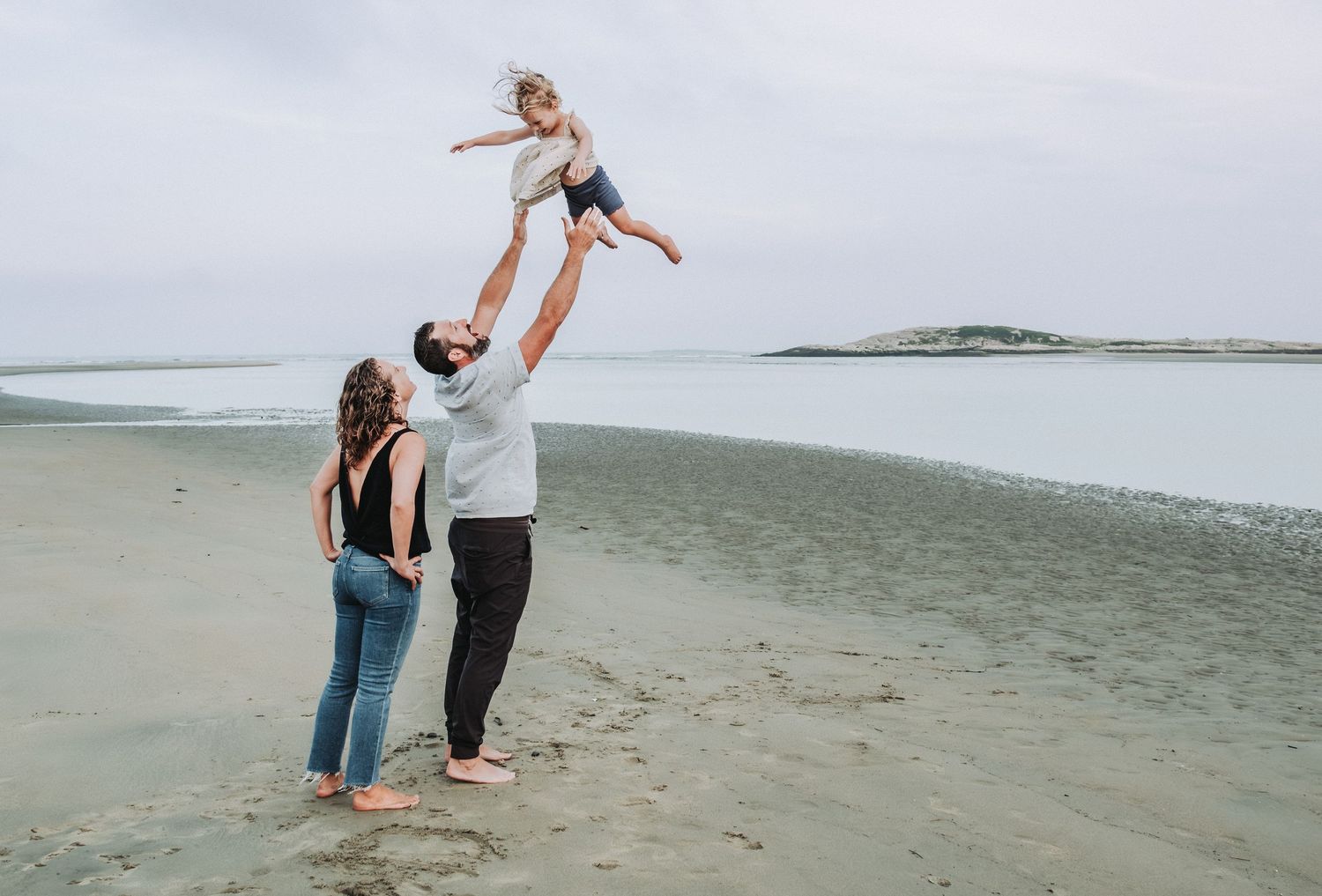 Family walking and playing together on a foggy beach during a cloudy day by the ocean.
