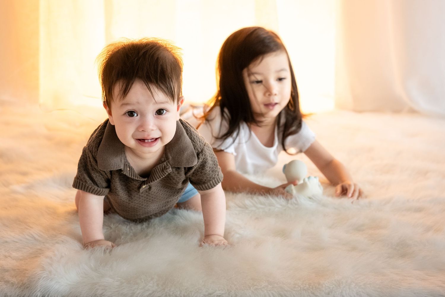 Two young children crawl and play together on a soft carpet in warm sunlit room.