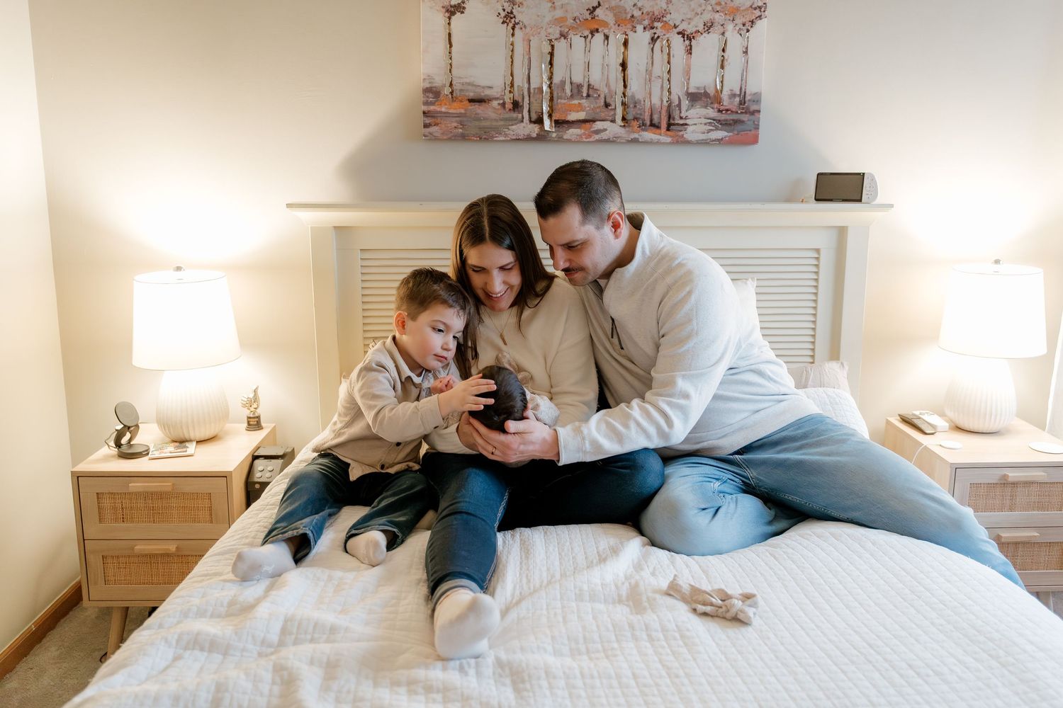 Family of three sitting on a bed, parents and young child looking at a small puppy together in a cozy bedroom.